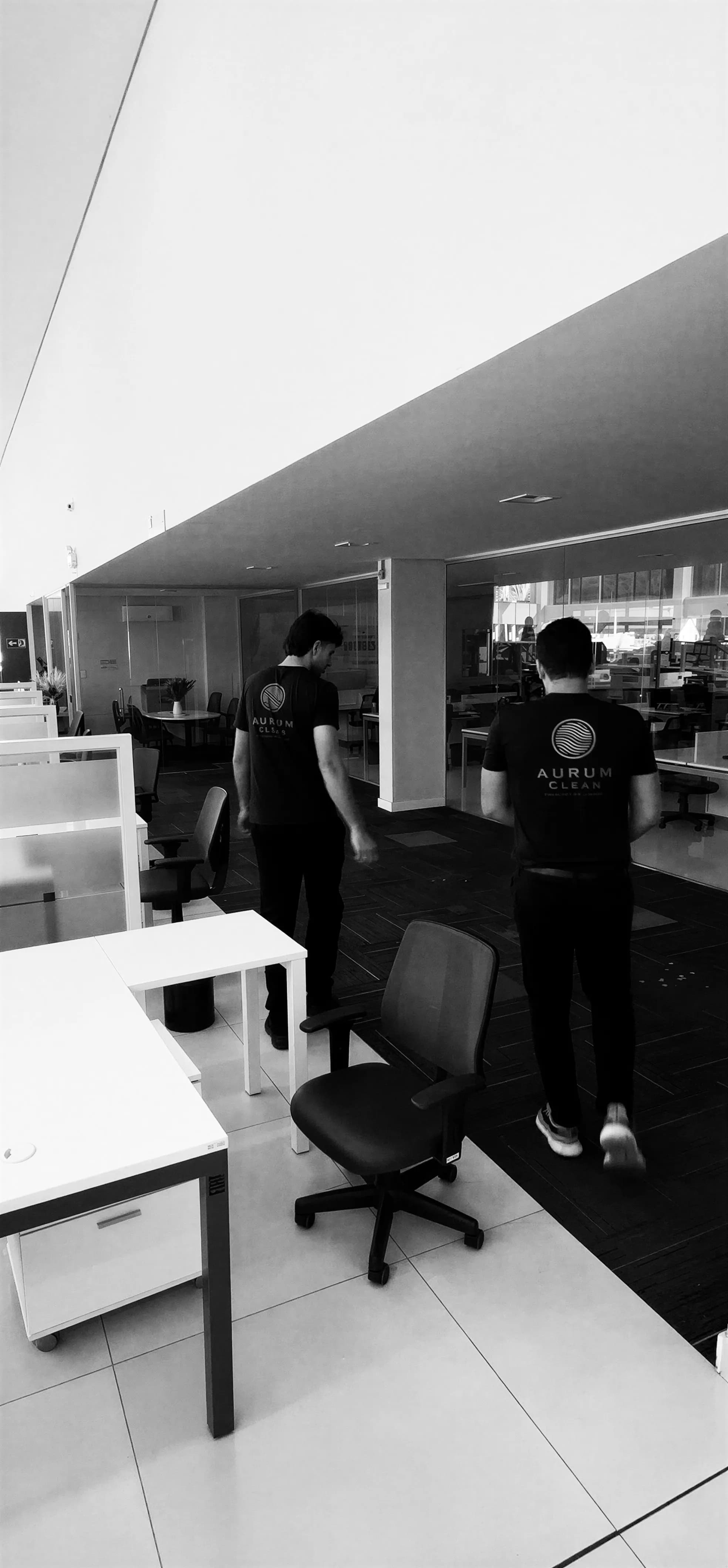 Dois técnicos da Aurum Clean caminhando por um escritório, em preto e branco